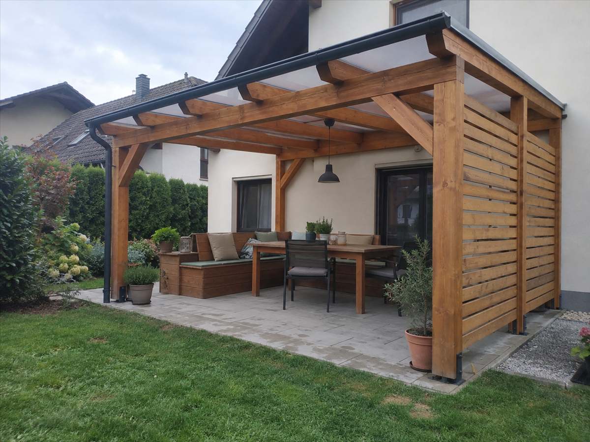 Pokrita pergola ob hiši z letveno steno in kotno klopjo
